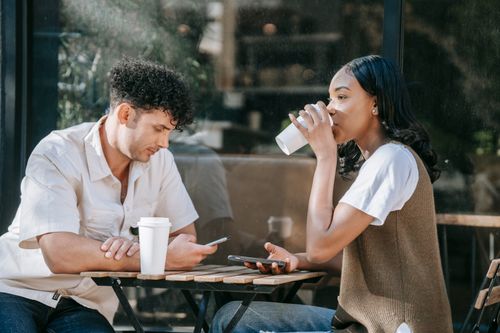 Free Two friends enjoying a casual coffee break outdoors. Close-up of a man and woman with smartphones. Stock Photo