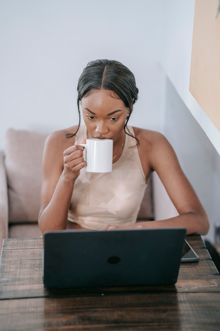 A Woman Sipping Coffee While Using A Laptop