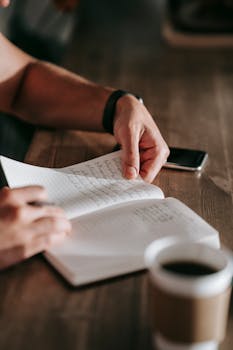 Close-up of a person journaling indoors with coffee, showcasing selective focus and depth of field.