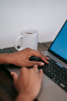 Close-up of hands typing on a laptop with a coffee cup nearby, indoors.