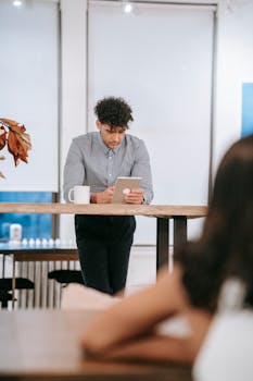 Young professional browsing tablet in casual office environment, focused and engaged.
