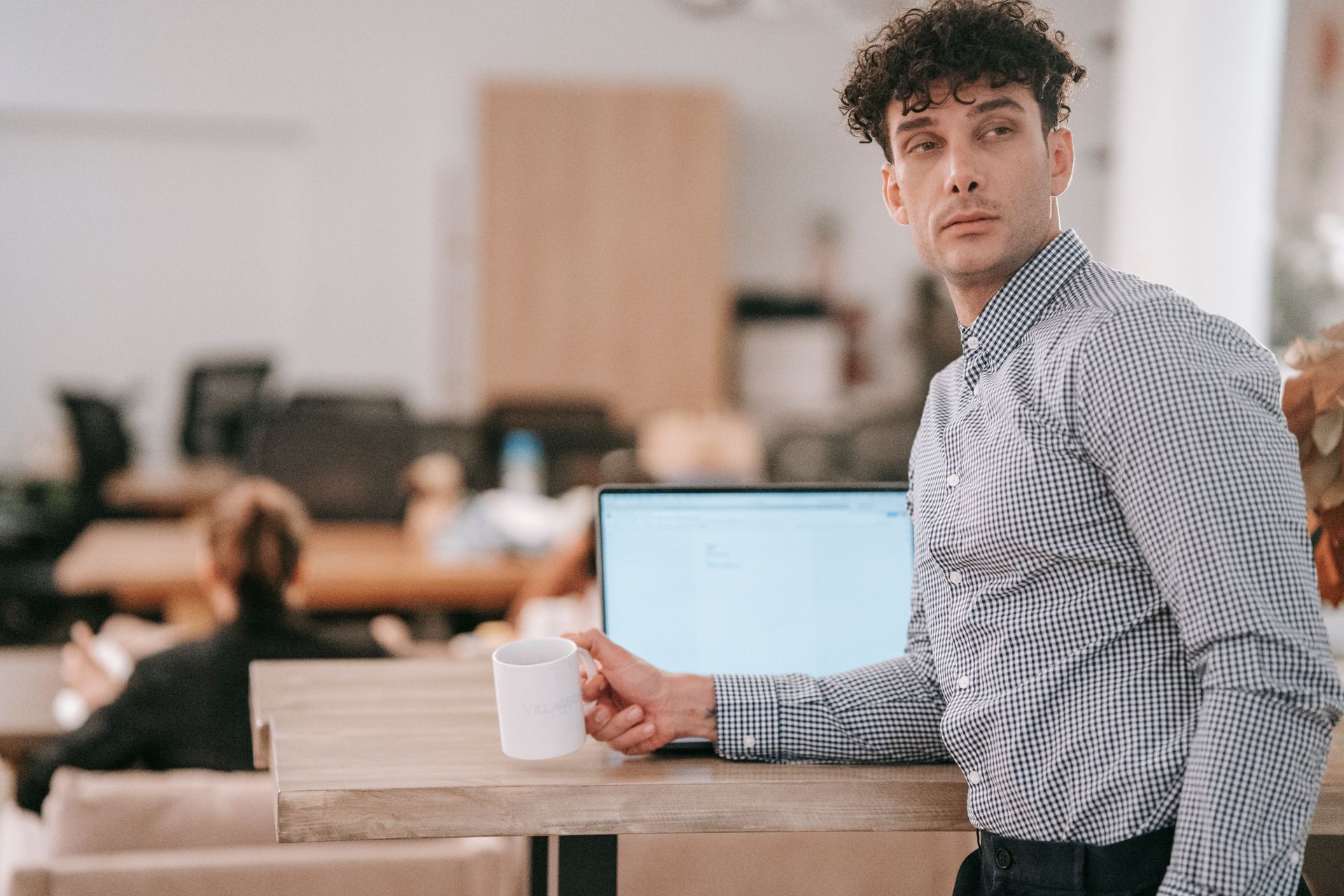 Stylish young man enjoying a hot drink while leaning on a desk in a modern office setting.