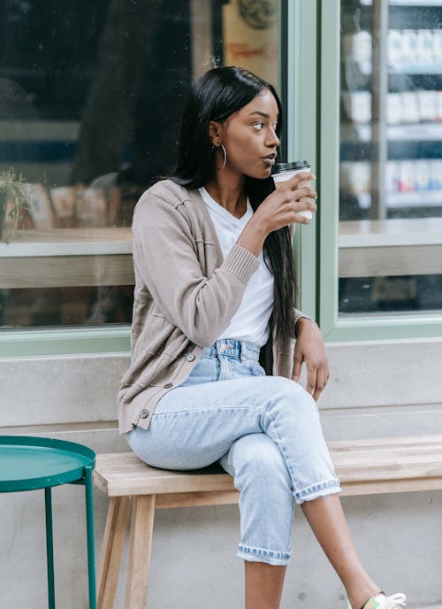A Woman Sipping Coffee While Sitting on a Wooden Bench