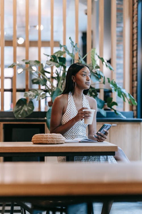Free A Woman Holding a Drink and a Cellphone While Sitting at a Table Stock Photo