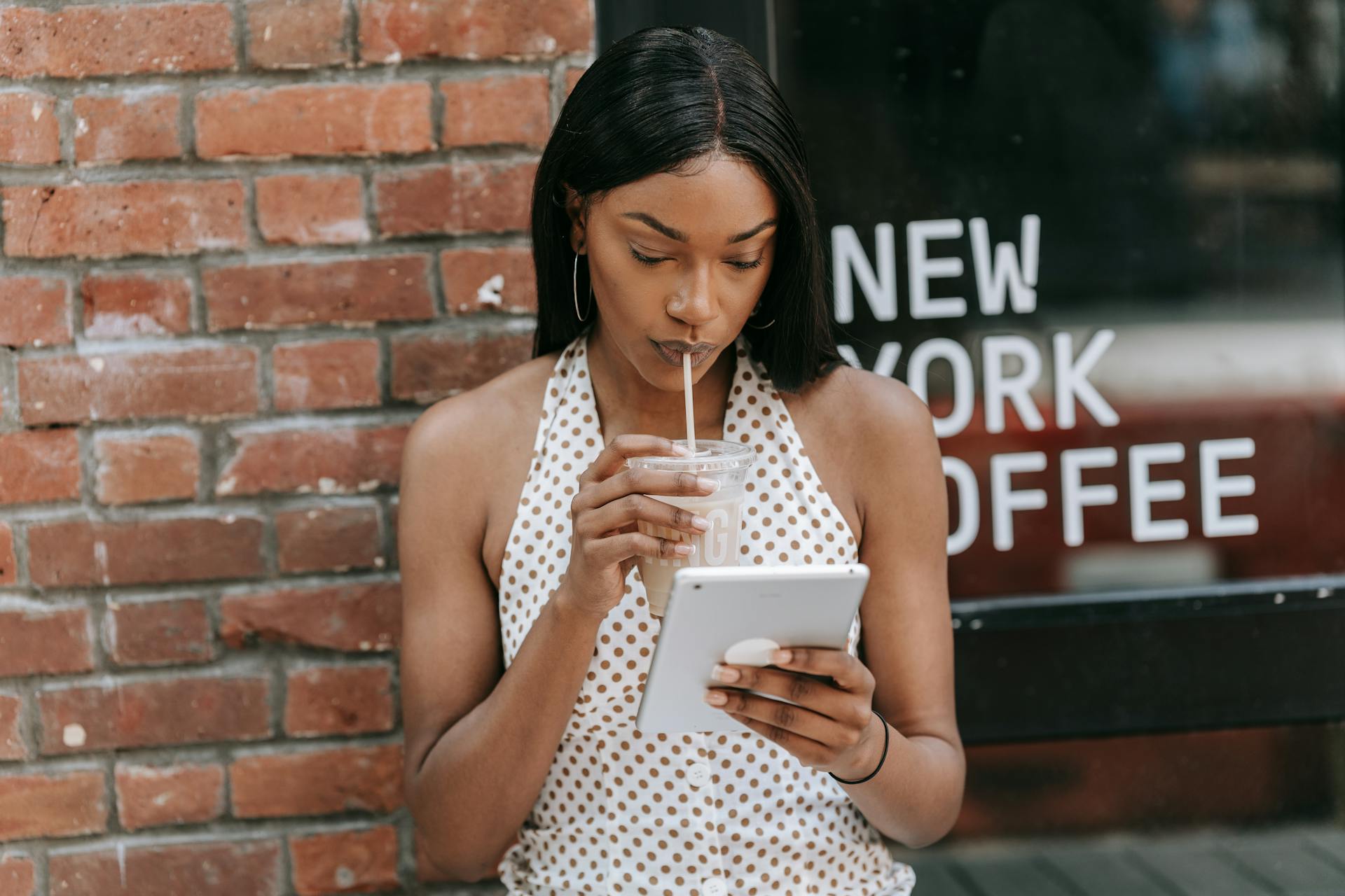 Woman sipping iced coffee and using a tablet outside a New York coffee shop.