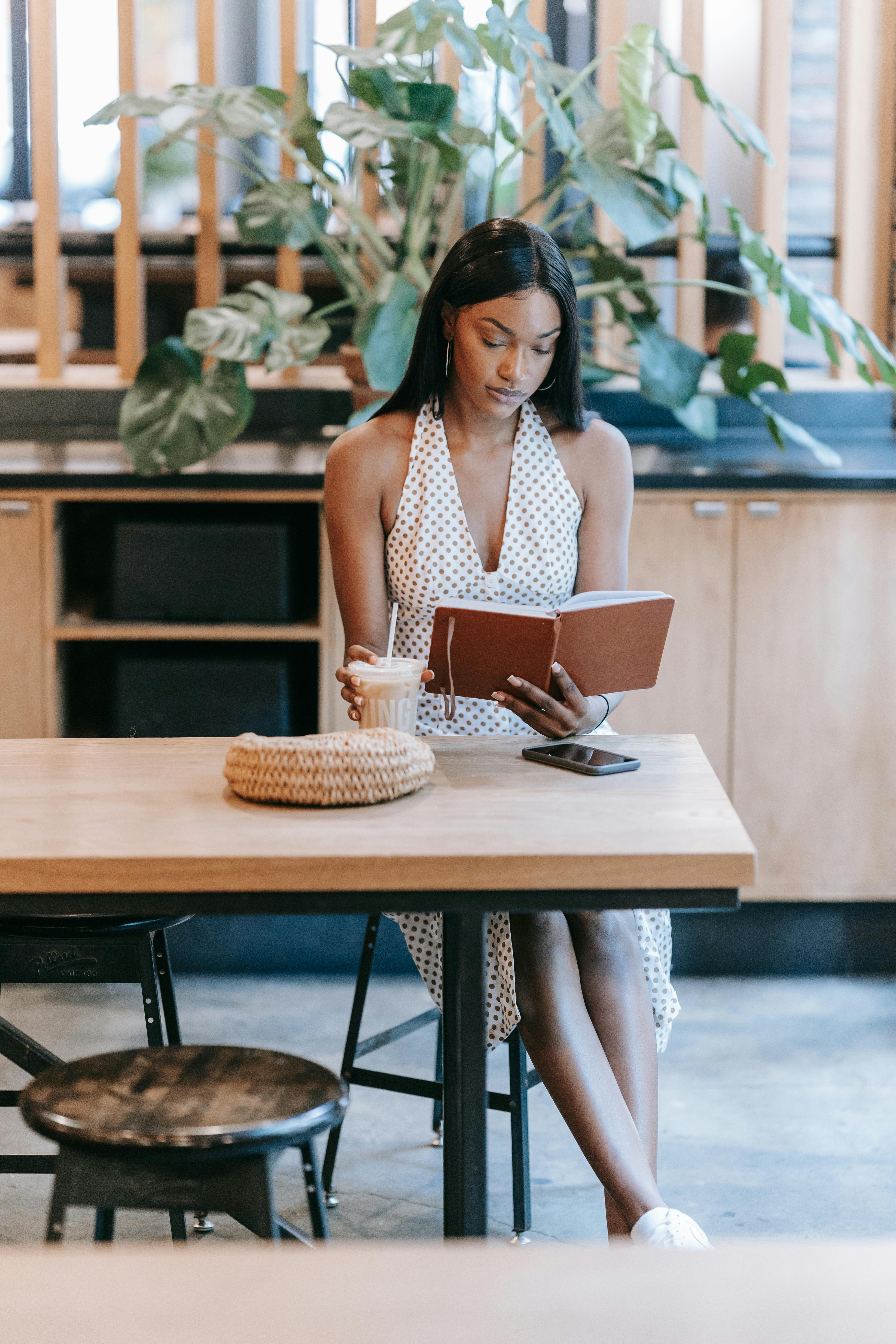 a woman in white sleeveless dress sitting on chair and reading a book