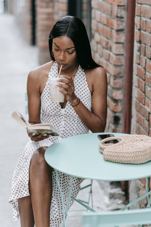 A Woman Reading a Book While Sipping a Drink