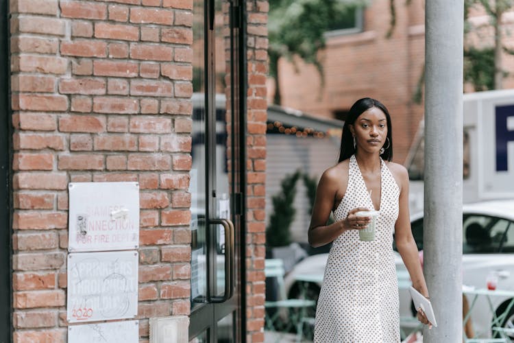 A Woman Walking Out Of A Cafe Holding A Drink And A Tablet