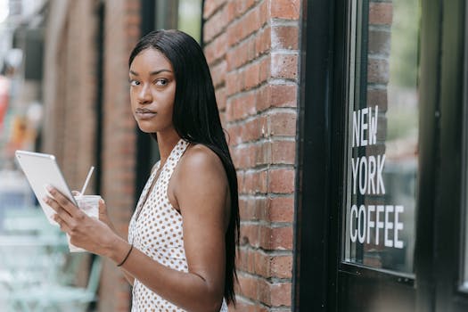 Stylish woman holding tablet and drink outside a New York coffee shop, blending modern technology and urban vibes.