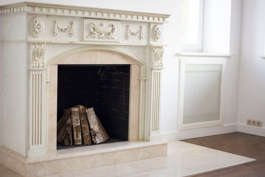 Elegant classic fireplace with firewood set in a bright, indoor home setting, surrounded by white walls and detailed craftsmanship.