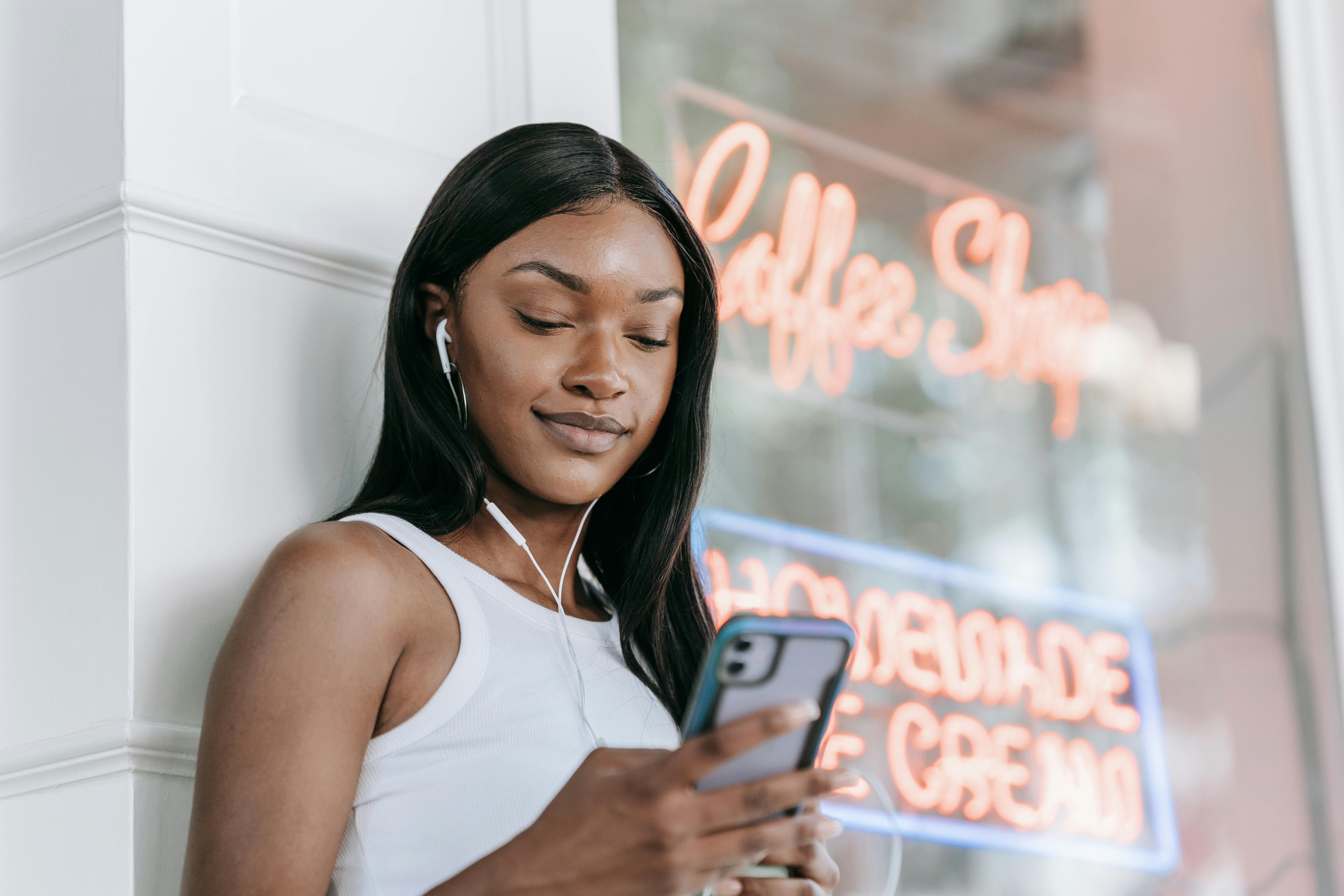 Smiling woman with earphones using smartphone outside a coffee shop.