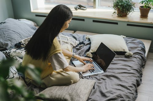 Free A Woman in Yellow Vest Using a Laptop in Bed Stock Photo