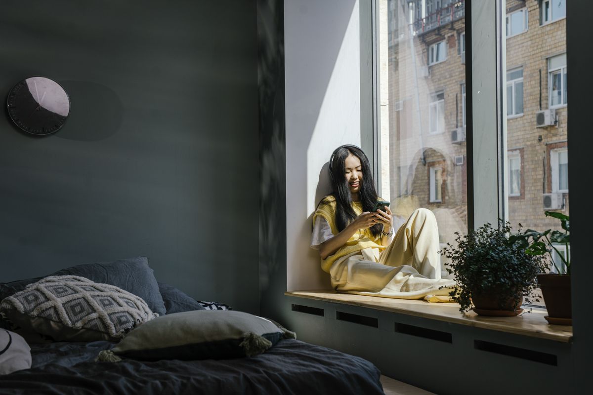 A woman sitting by a window smiling at her phone