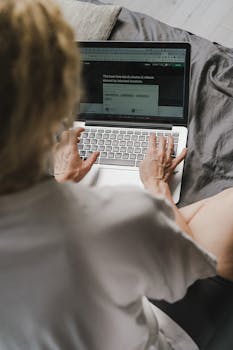 A woman typing on a laptop while sitting comfortably at home, viewed from behind.