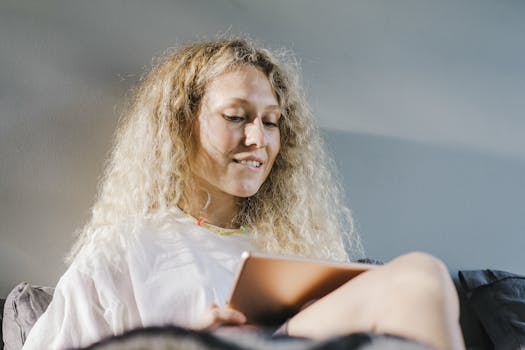 Smiling woman with curly blonde hair using a tablet indoors, enjoying relaxed time.