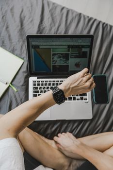 An individual checks their smartwatch while using a laptop, surrounded by a notebook and a smartphone.