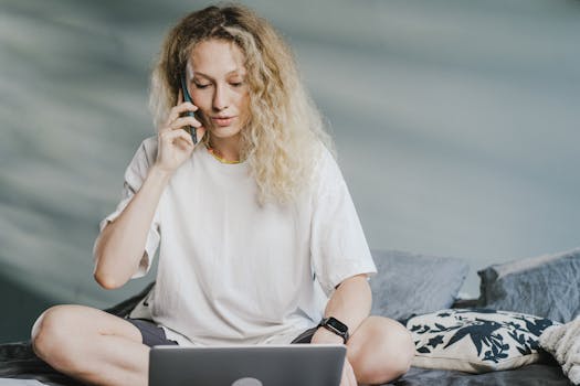 Young woman multitasking at home on laptop and phone call.