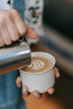 A close-up of a barista pouring milk to create latte art in a cup of coffee.