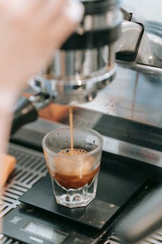 Espresso shot being freshly brewed into a glass cup from a coffee machine.