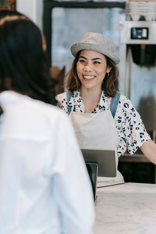 Free Smiling female barista in apron and hat serves customer in cafe. Stock Photo