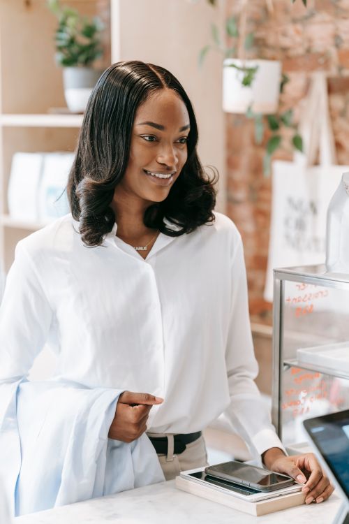 Free A woman in a white shirt smiles at a store counter, creating a warm and welcoming atmosphere. Stock Photo