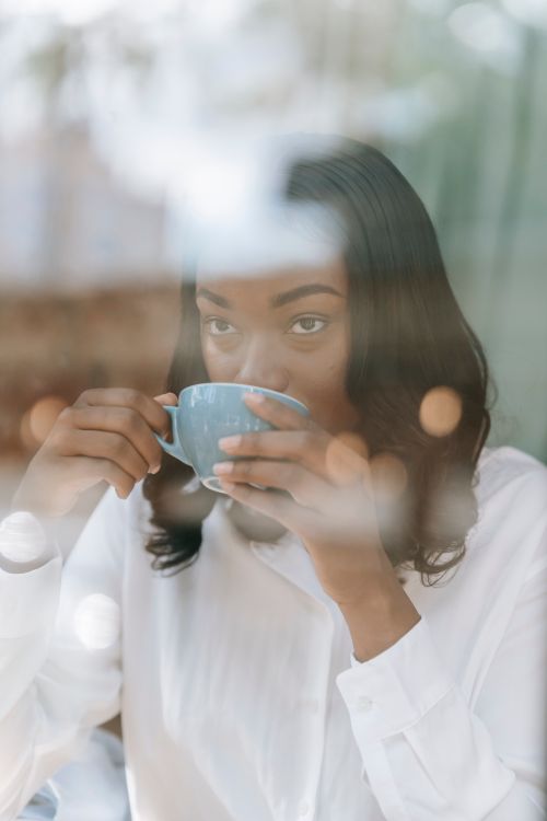 Free A woman enjoys a cup of coffee indoors, captured through a glass with reflections. Stock Photo