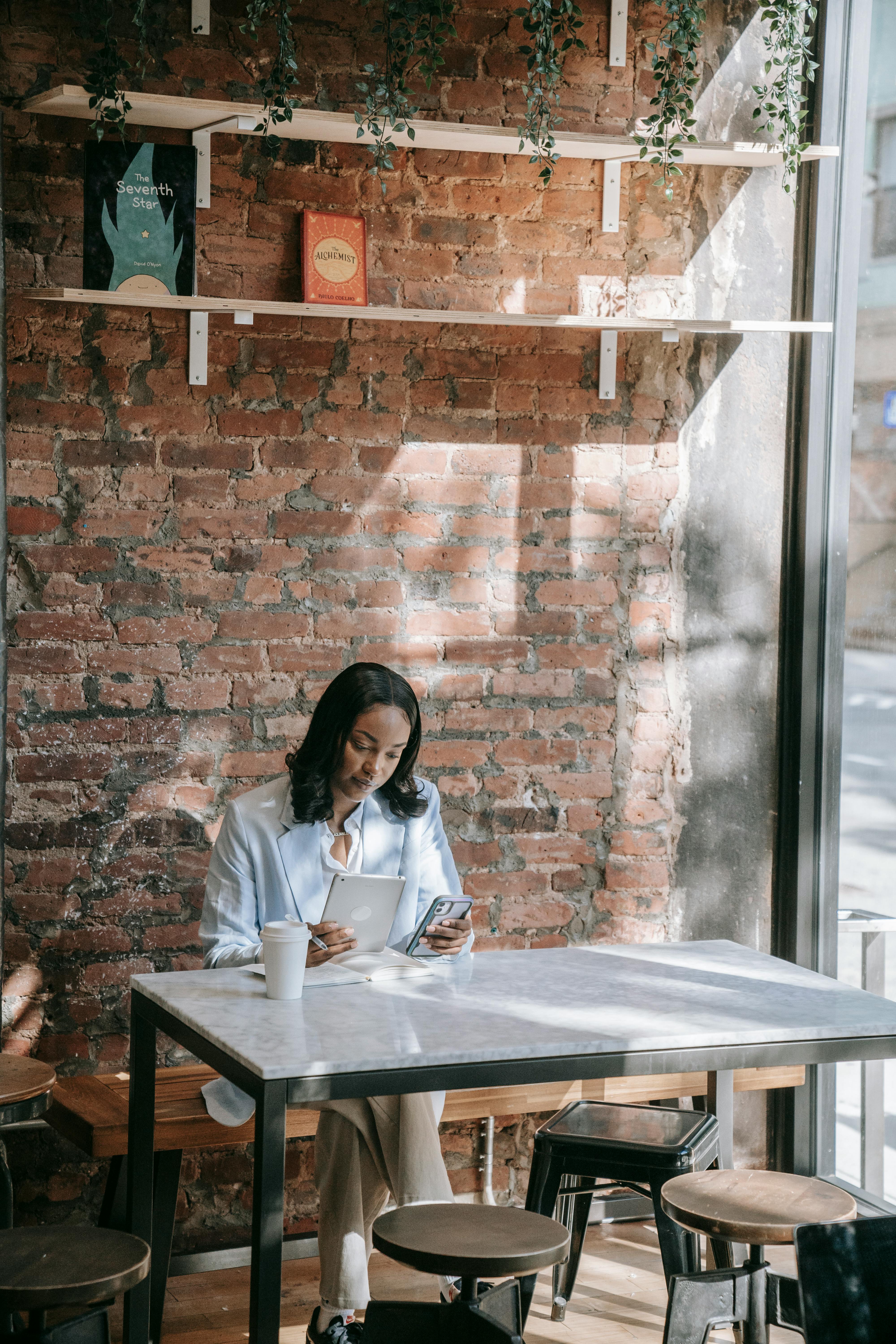 A professional woman multitasking with a smartphone and tablet in a stylish cafe setting.