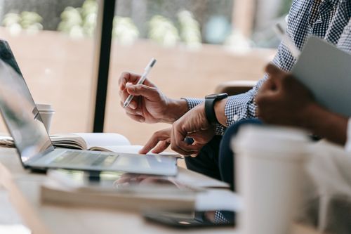 Free Close-up of colleagues discussing work using a laptop and notebook in an indoor office setting. Stock Photo