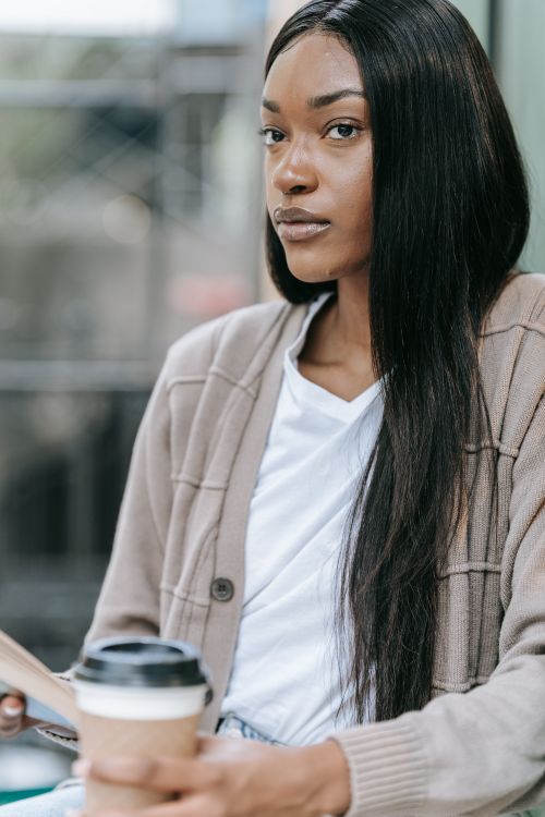 Free Stylish woman holding coffee cup, looking thoughtful in a city cafe. Stock Photo