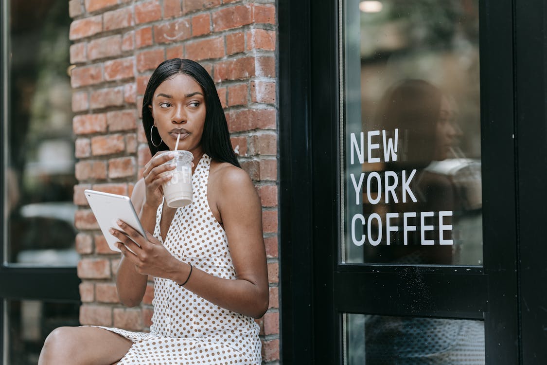Woman in White and Brown Polka Dot Sleeveless Dress Drinking Iced