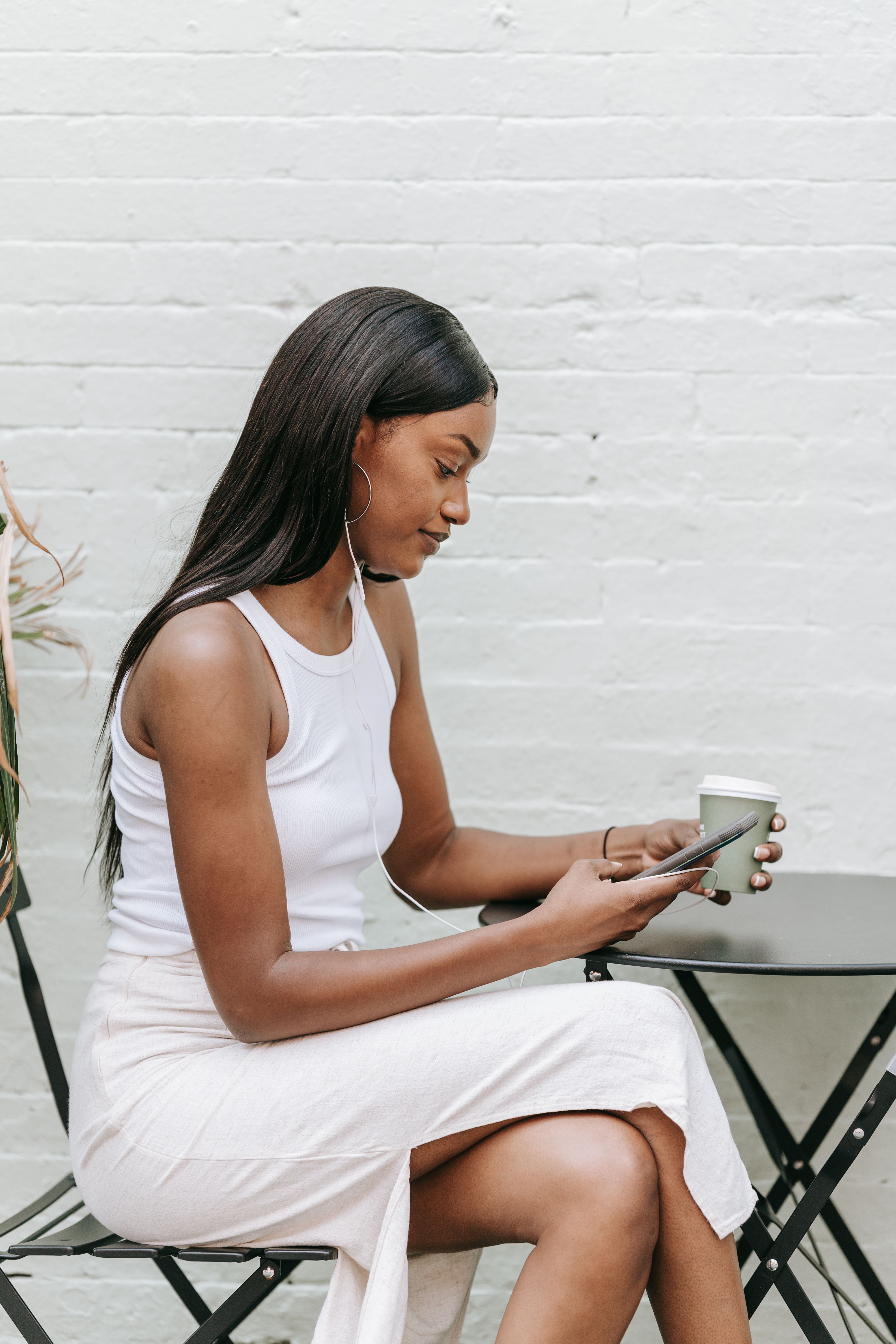 A woman enjoys coffee and her smartphone at an outdoor café table, in a calm setting.