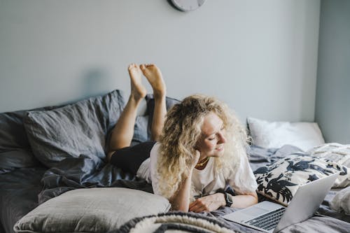 Blonde Woman in White Shirt Lying on Bed Watching on Laptop