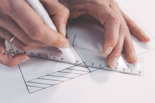 Close-up of hands drawing precise lines with ruler and pen, emphasizing accuracy.