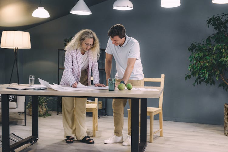 Man And Woman Leaning Over A Table And Working On A Project 