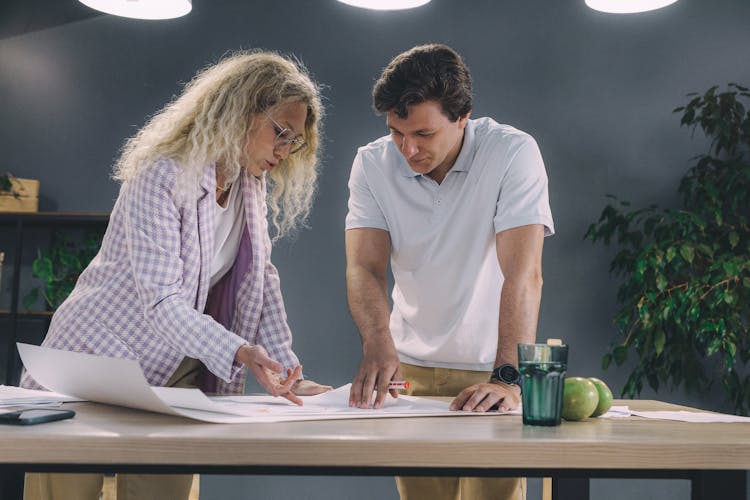 Man And Woman Leaning Over A Table And Working On A Project