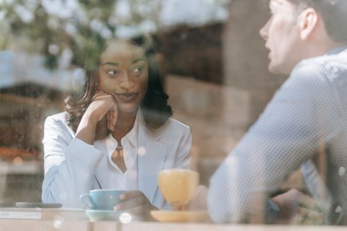 Free An African American woman and a man sit at a cafe, enjoying a conversation over coffee. Stock Photo