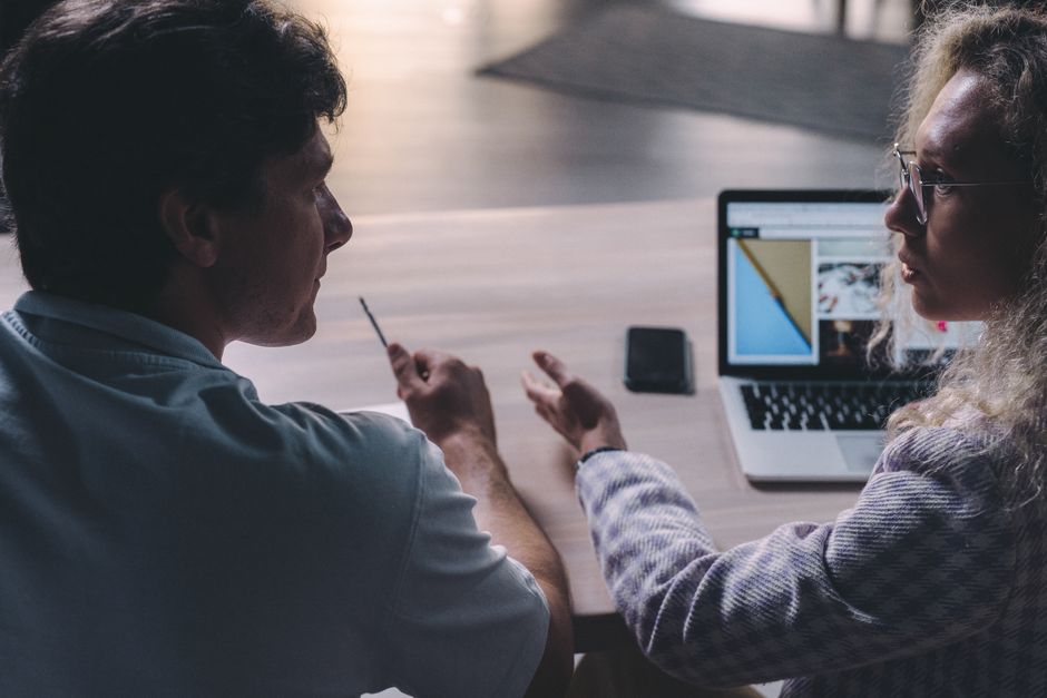 Two colleagues having a serious discussion, reviewing content on a laptop in a modern office.