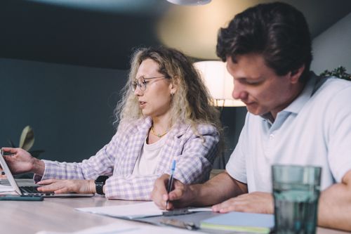 Free Two colleagues collaborating at a desk with laptops and papers in a modern office setting. Stock Photo