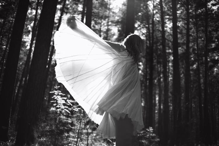 Grayscale Photo Of Woman In White Dress Standing In Forest