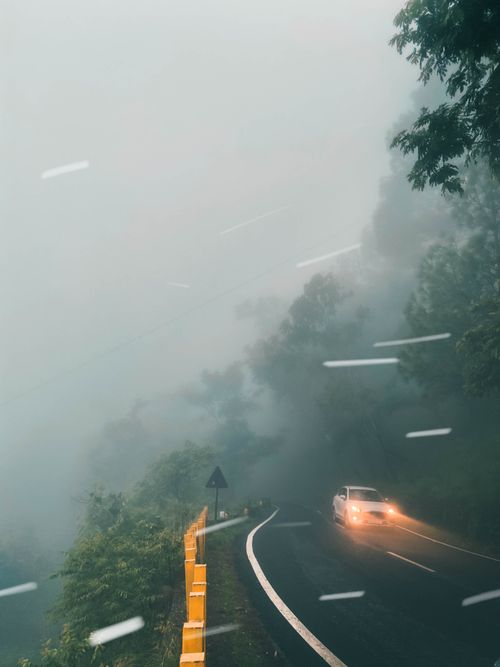 Free A solitary car navigates a foggy, winding mountain road, creating an eerie atmosphere. Stock Photo