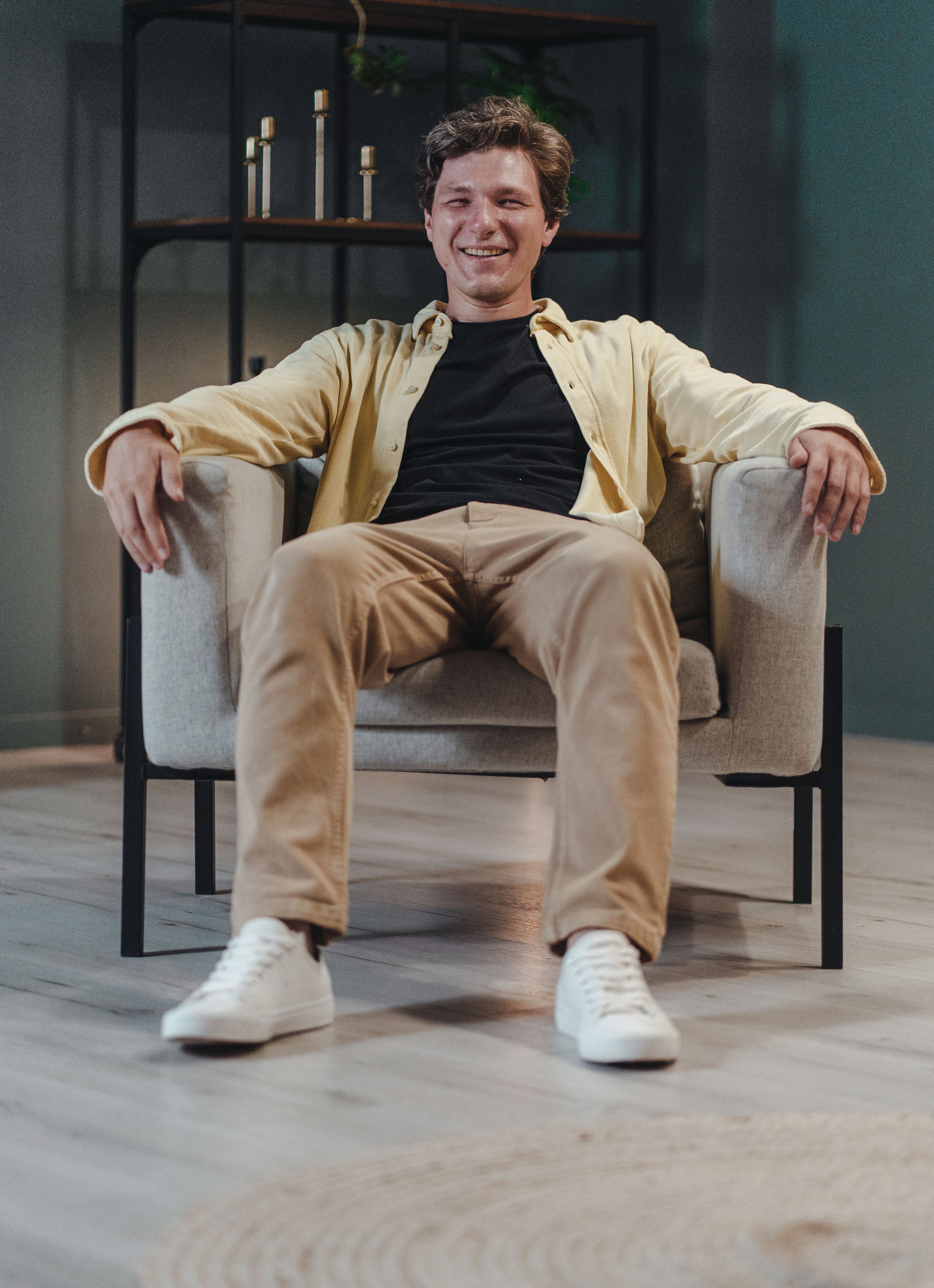 Smiling man in casual outfit sitting comfortably in a modern armchair, interior setting.
