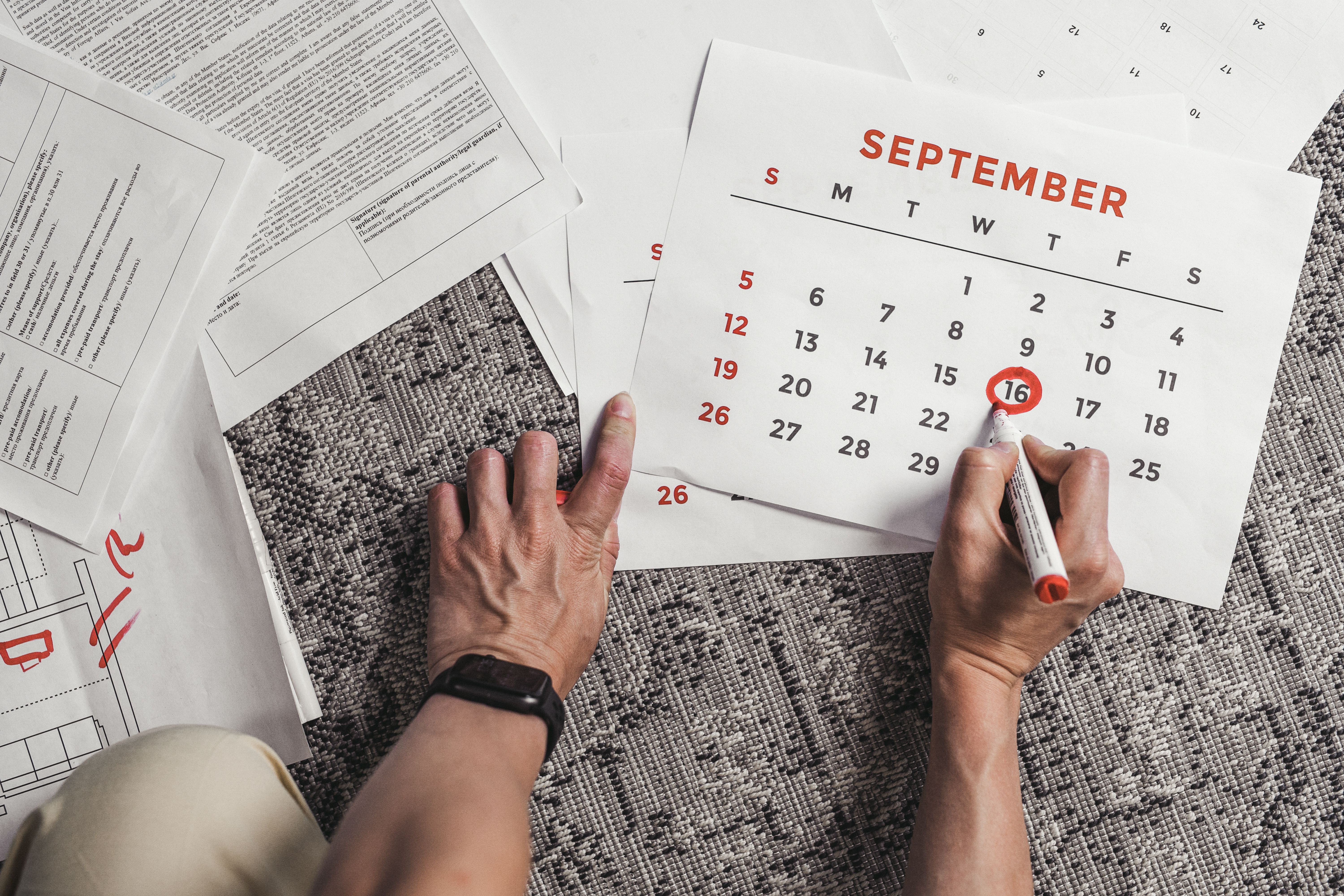 Person circling a date on a September calendar beside scattered documents.