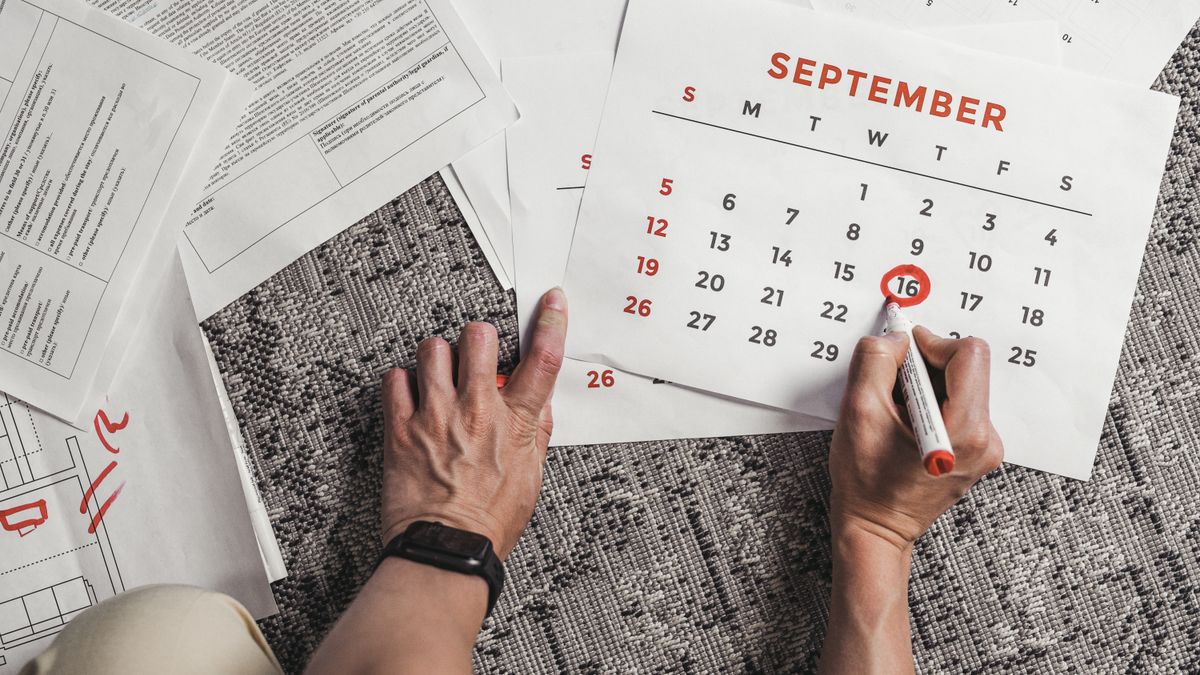 9月のカレンダーの日付に赤いペンで印を付けている手元。まわりに書類が広げられている