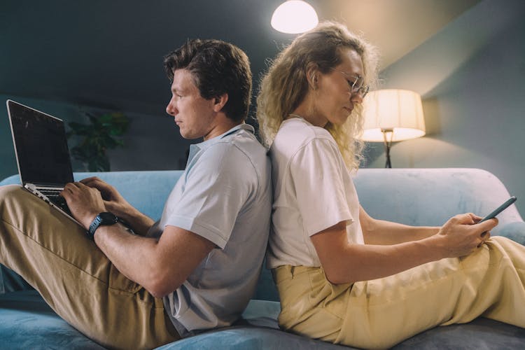 A Couple Sitting Back To Back On A Blue Sofa