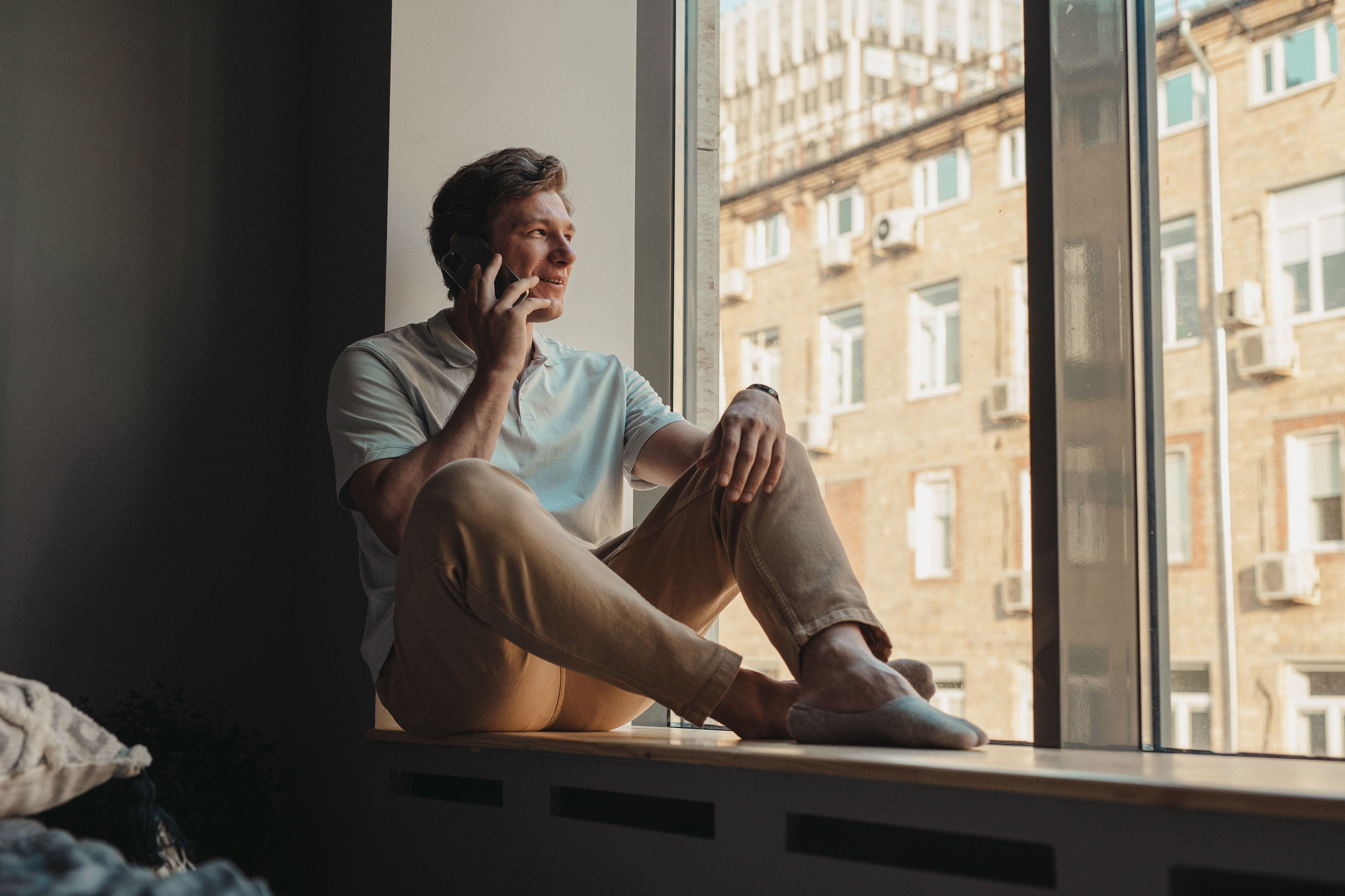 person sitting cross-legged on a couch with a phone in their lap, looking contemplative