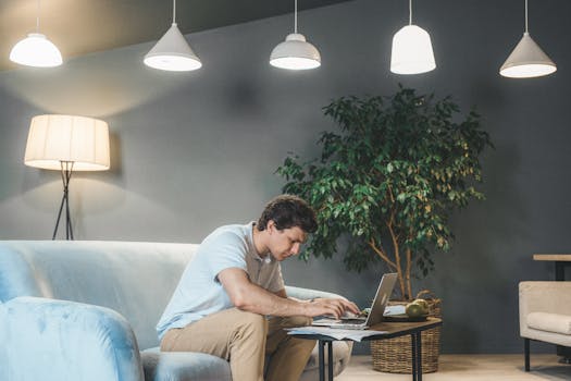 A man working on a laptop in a cozy living room setting with a sofa and a wooden table.