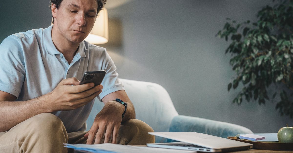 Person sitting on a sofa reading news on a phone with a serious expression