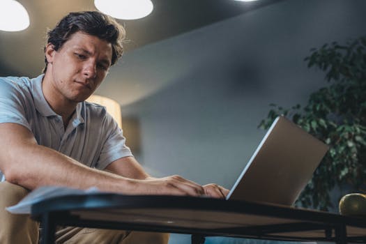 Adult man concentrating while working on a laptop indoors, in a modern office setting.