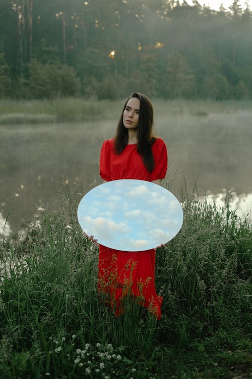 Free Woman Standing in Green Grass Carrying a Round Mirror  Stock Photo