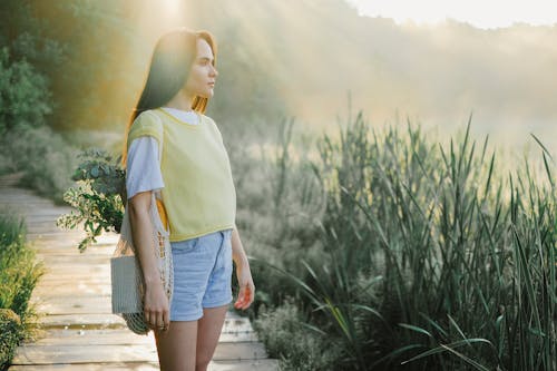 Woman in Yellow Shirt and Blue Denim Shorts Standing on Brown Wooden Pathway